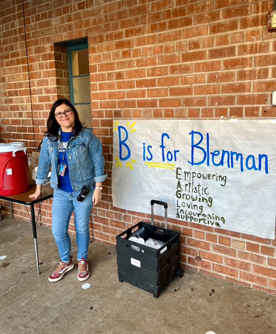 A teacher poses next to the B is for Blenman poster