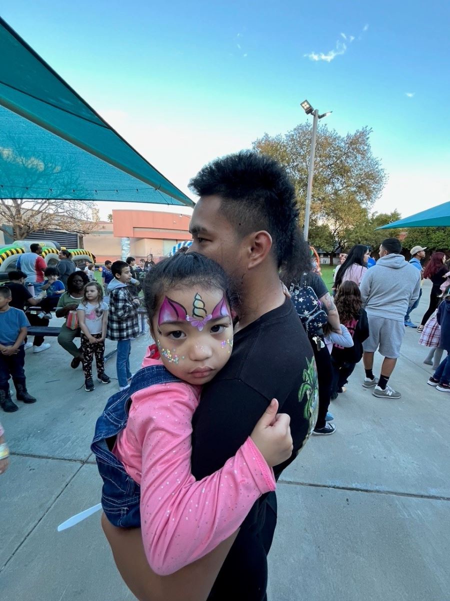 A dad holds his little girl to show off her face paint